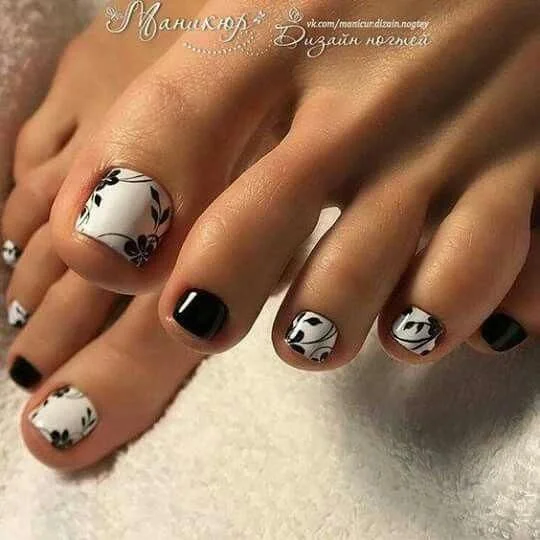 Black and White Nail Designs 2025: Chic Ideas for Every Occasion 14 Black and white floral pedicure design featuring glossy polish with alternating solid black and white nails, accented by delicate black flower patterns for a chic and stylish toe nail look.