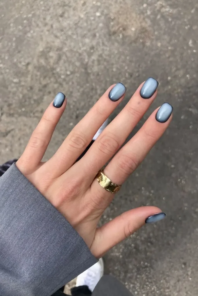 Short square nails featuring a trendy blue aura nail design with a black border, creating a misty, faded look over a pale blue color.
