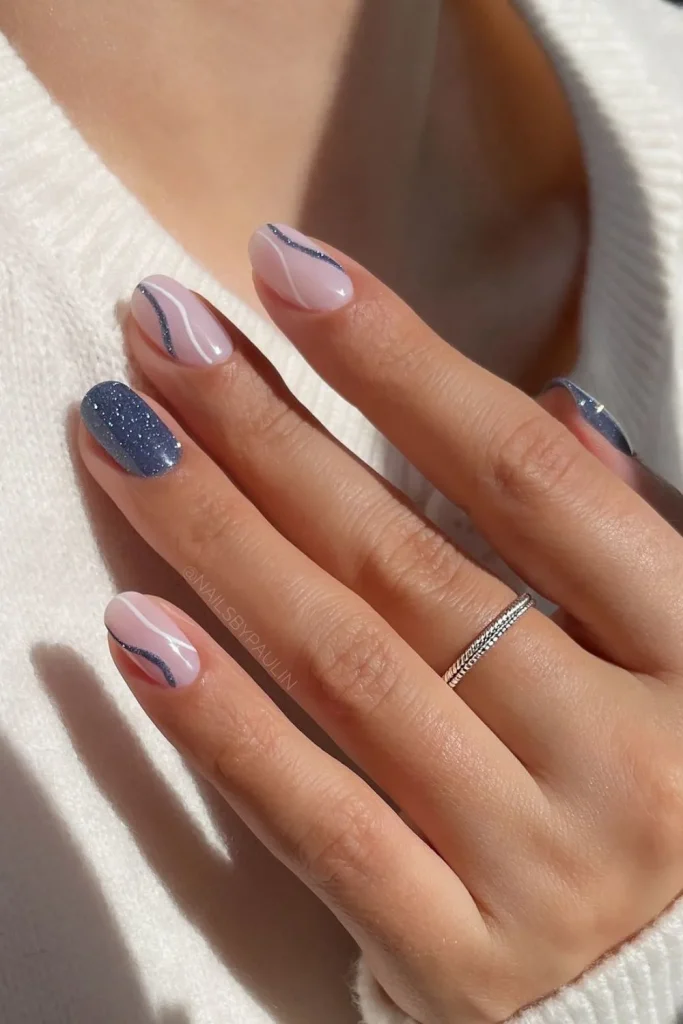 Short oval nails with a milky pink base featuring white and blue glitter wavy lines for a soft, modern manicure.