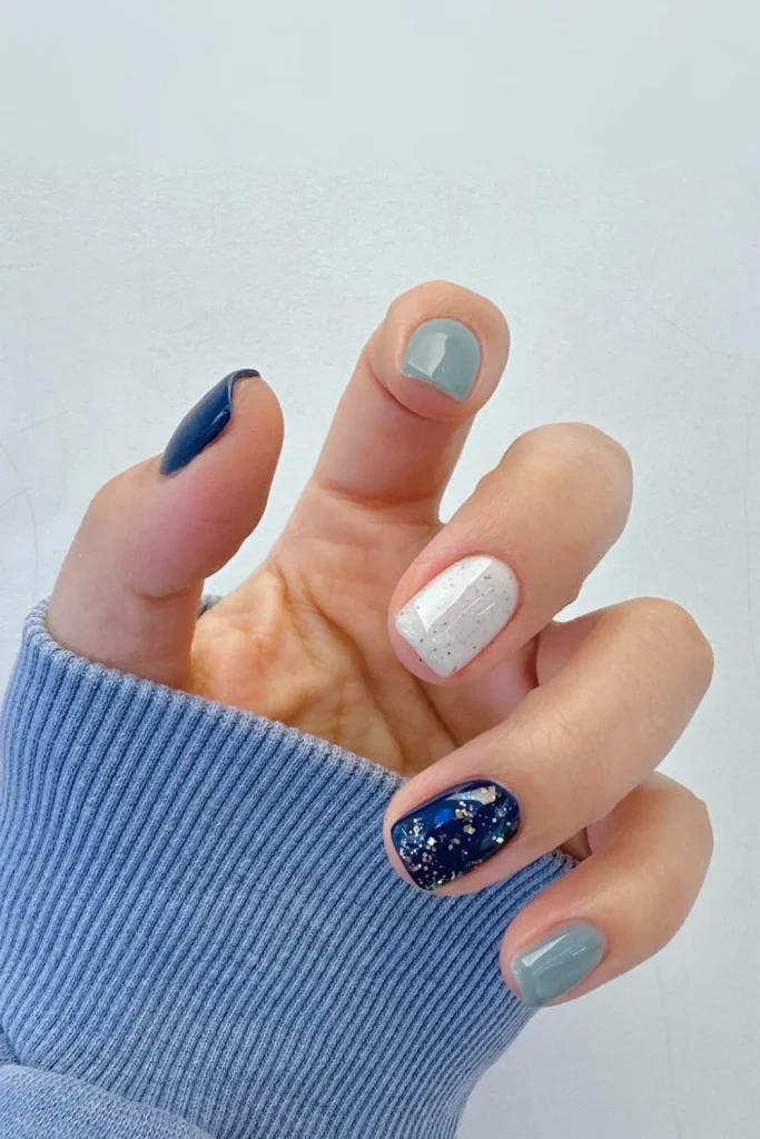 Skittle manicure combining solid blue, white glitter, and light blue shimmer on rounded square nails
