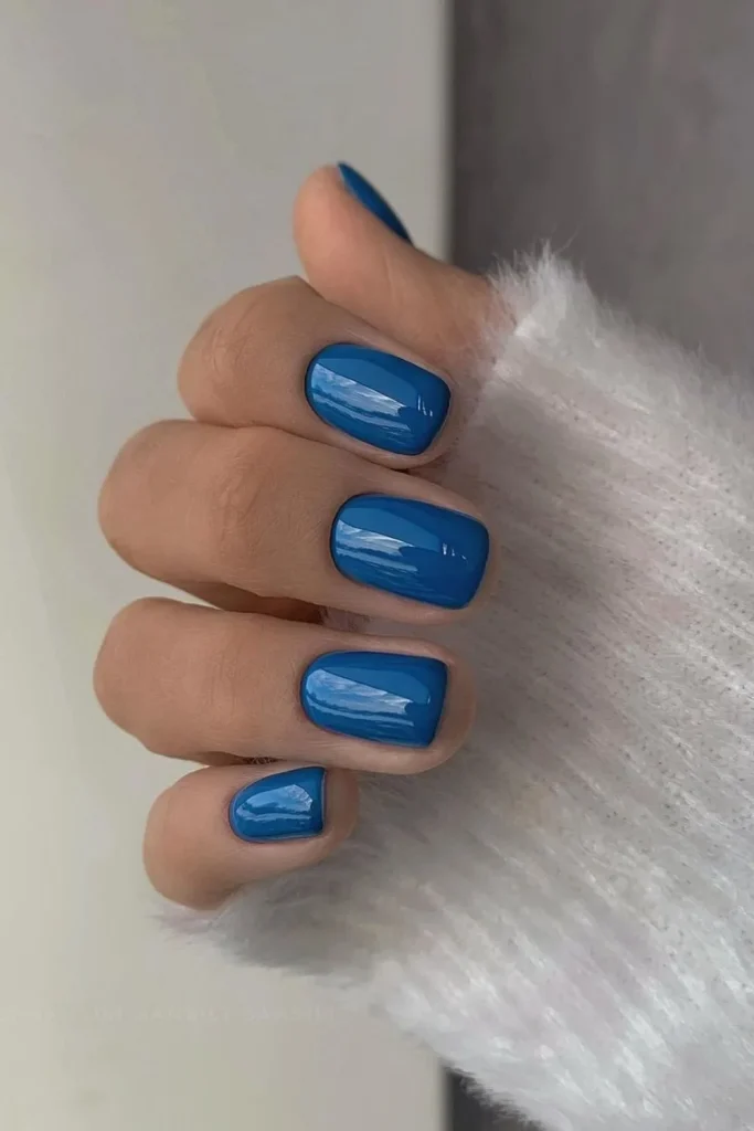 Short square-round nails painted in a solid, vibrant, and glossy cobalt blue polish color, perfect for a summer or spring manicure.