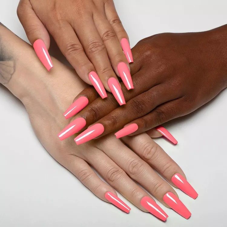 32+ Best Nail Colors for Dark Skin That Look Absolutely Stunning 18 Two hands with different skin tones (light and deep brown) showcasing long, bright coral pink coffin/ballerina nails. The vibrant pink color is high-gloss and striking on both complexions.