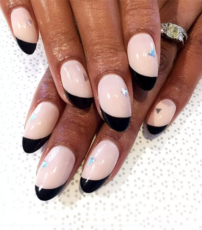 51 Easy Nail Designs You Can Do at Home (Even if You’re a Total Beginner) 45 Hands with oval nails featuring a sheer pink base and a thick diagonal black French tip, accented with a single holographic triangle sticker near the cuticle.
