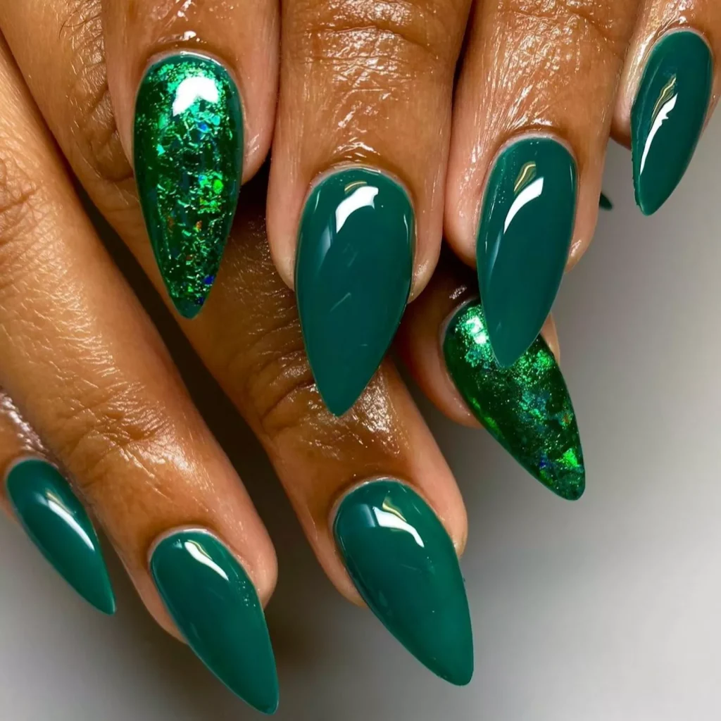 51 Easy Nail Designs You Can Do at Home (Even if You’re a Total Beginner) 7 Close-up of long, stiletto-shaped acrylic nails painted in a deep glossy emerald green with chunky dark green glitter accent nails.
