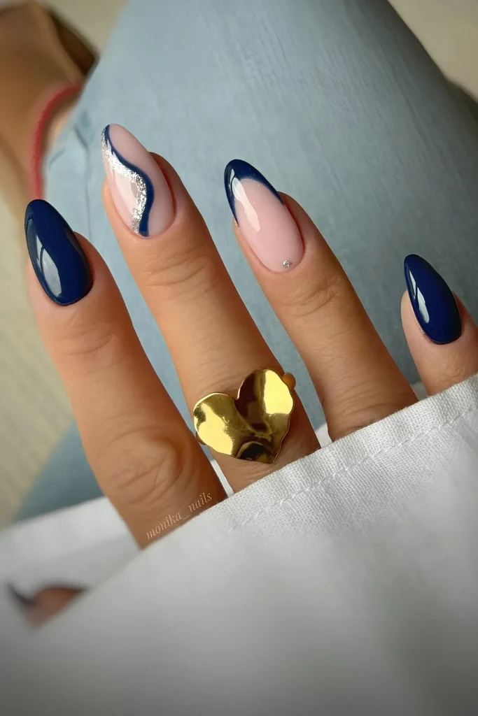 Long almond nails with a deep navy French tip and an abstract swirl of silver glitter and white on the accent finger.