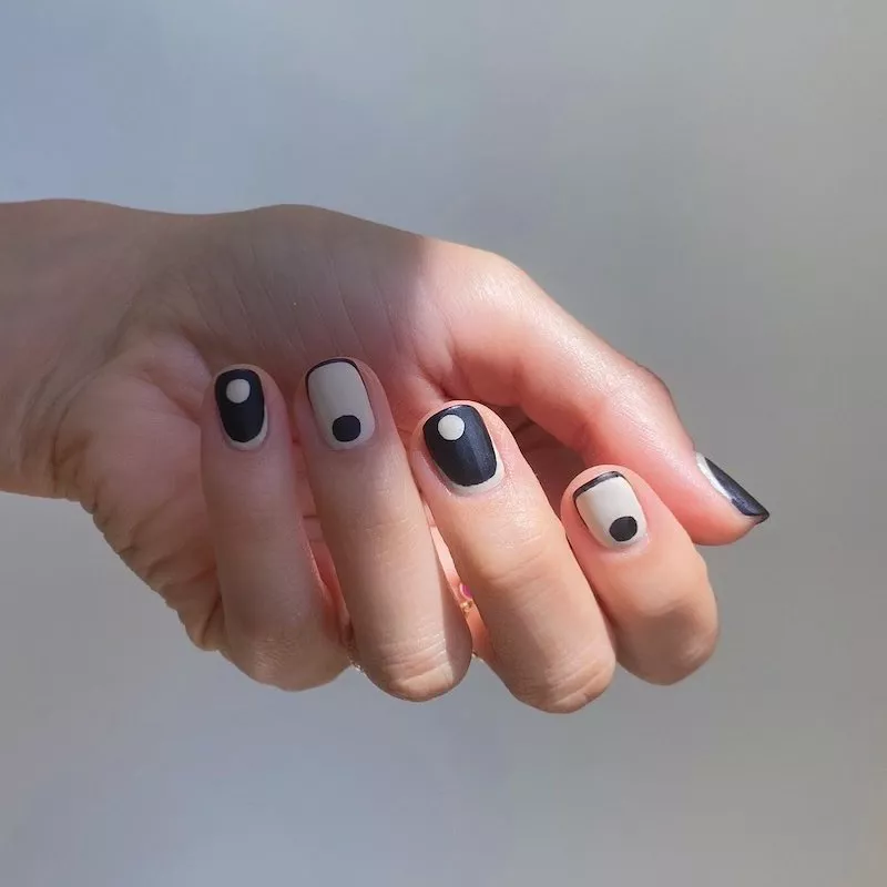 51 Easy Nail Designs You Can Do at Home (Even if You’re a Total Beginner) 48 Hand with short, square nails featuring a bold black and nude color-block design with contrasting white or black dots on each nail.