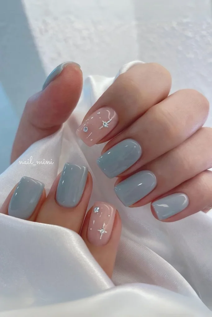Short square winter nails with solid dusty blue polish and pink accent nails featuring snowflake star rhinestones