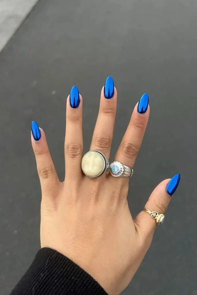 Long stiletto almond nails coated in a vivid, high-shine electric blue chrome or metallic blue gel polish.
