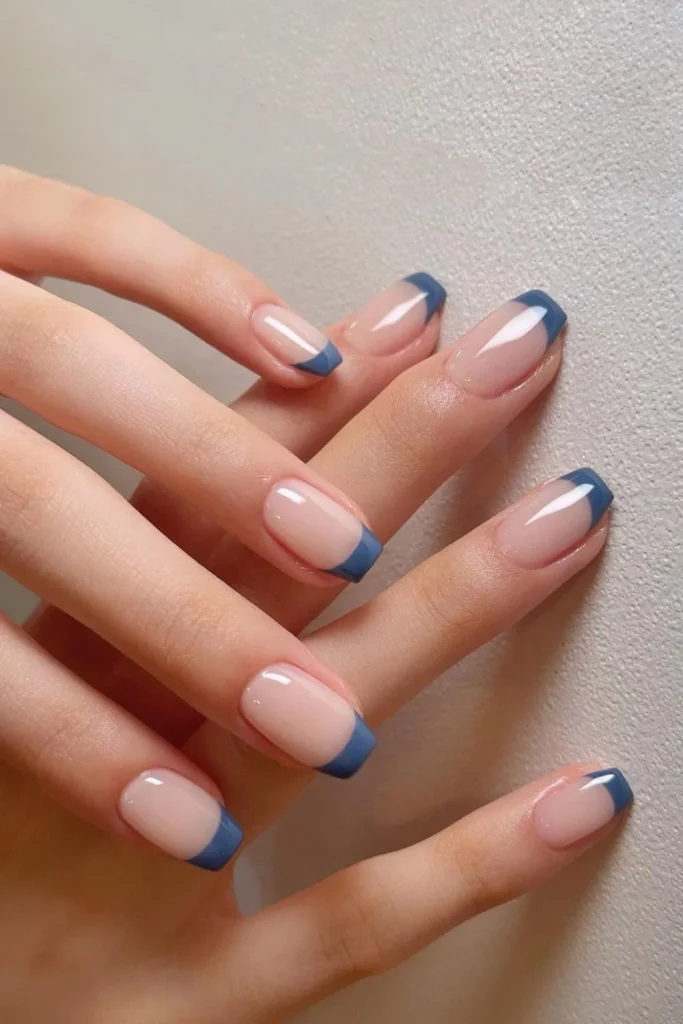 Short, neatly filed nails with a classic square French tip using a deep midnight blue polish on a sheer pink nude base.