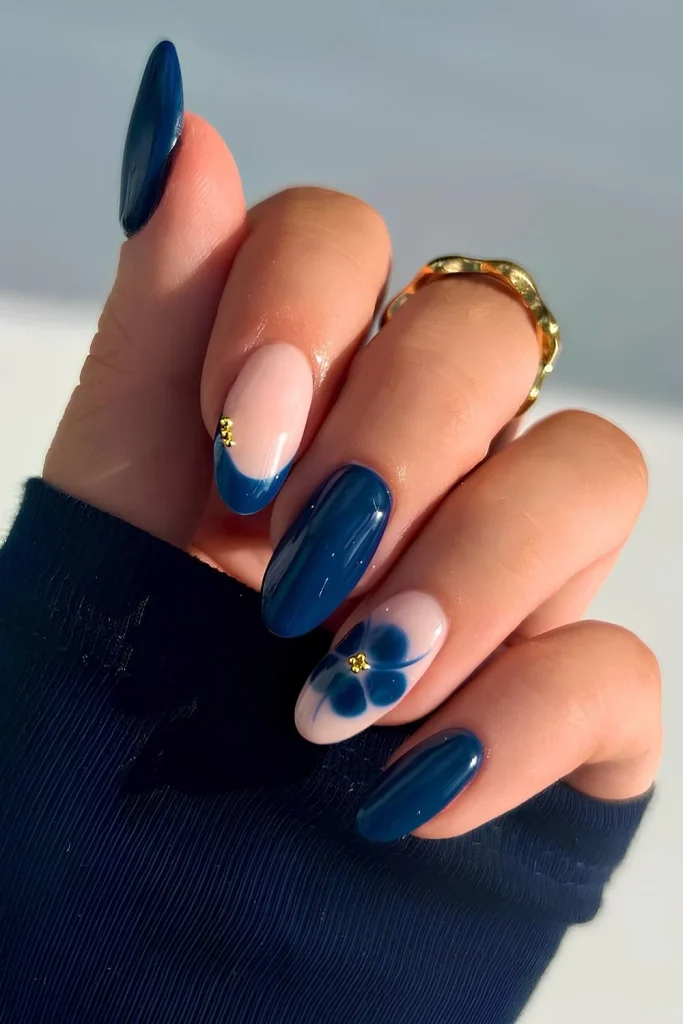 Dark blue almond nails with an accent nail featuring a navy blue blooming gel flower and a delicate gold bead design.