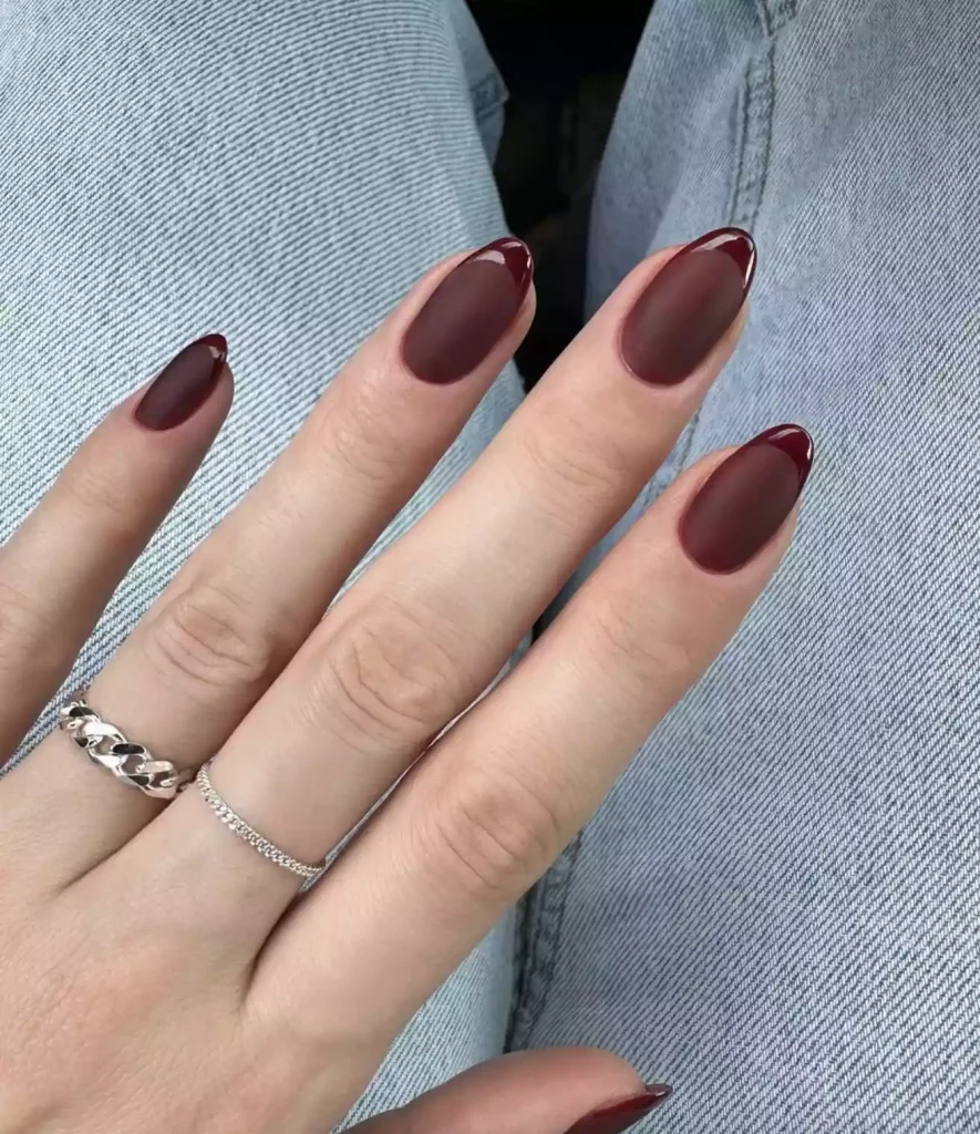 51 Easy Nail Designs You Can Do at Home (Even if You’re a Total Beginner) 40 Hand resting on blue jeans, showcasing long almond-shaped nails painted in a deep matte burgundy/wine red with a subtle glossy dark outline around the edges, known as the "Velvet" effect.