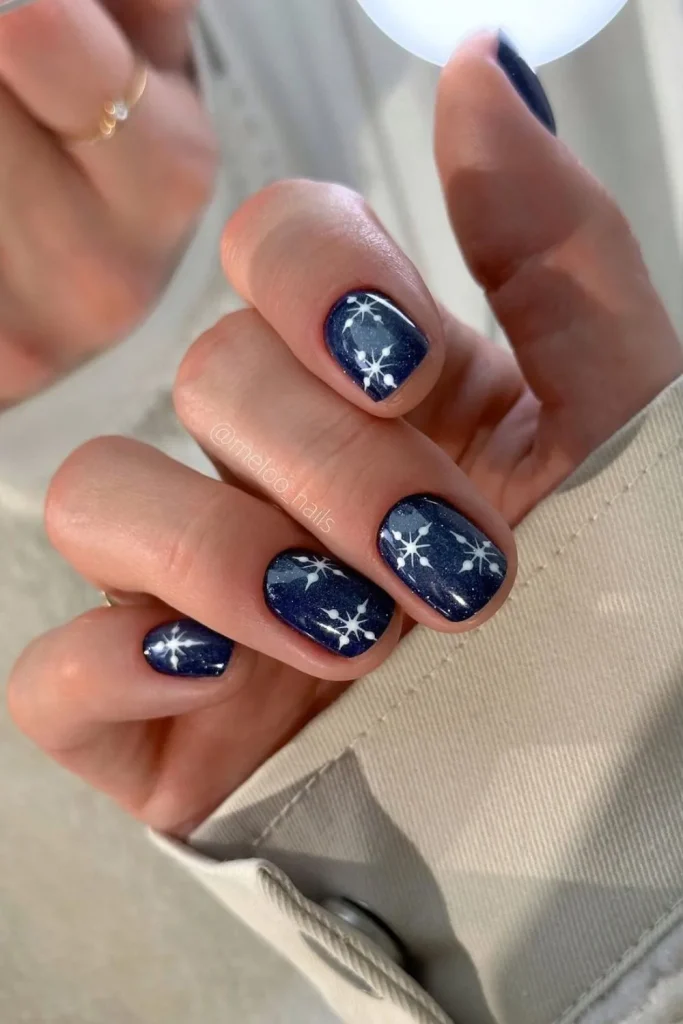 Deep navy blue almond nails with delicate silver glitter snowflake accent art