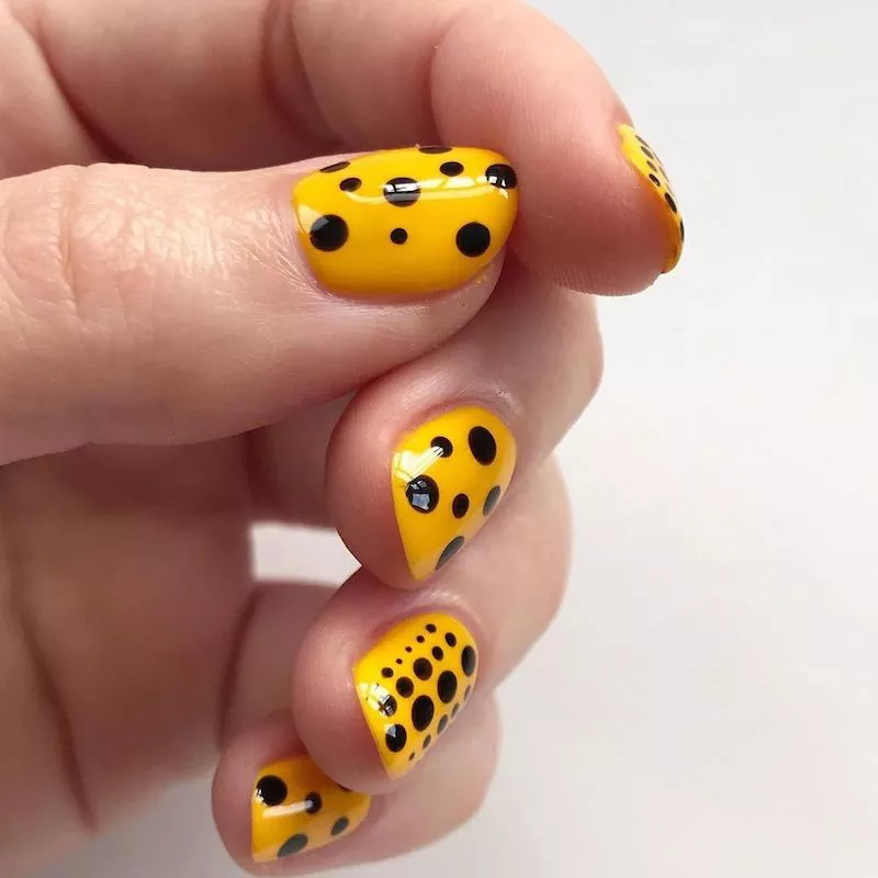 51 Easy Nail Designs You Can Do at Home (Even if You’re a Total Beginner) 33 Close-up of short, square nails painted a bright yellow base with large, randomly sized black polka dots covering the entire surface, inspired by the art of Yayoi Kusama.