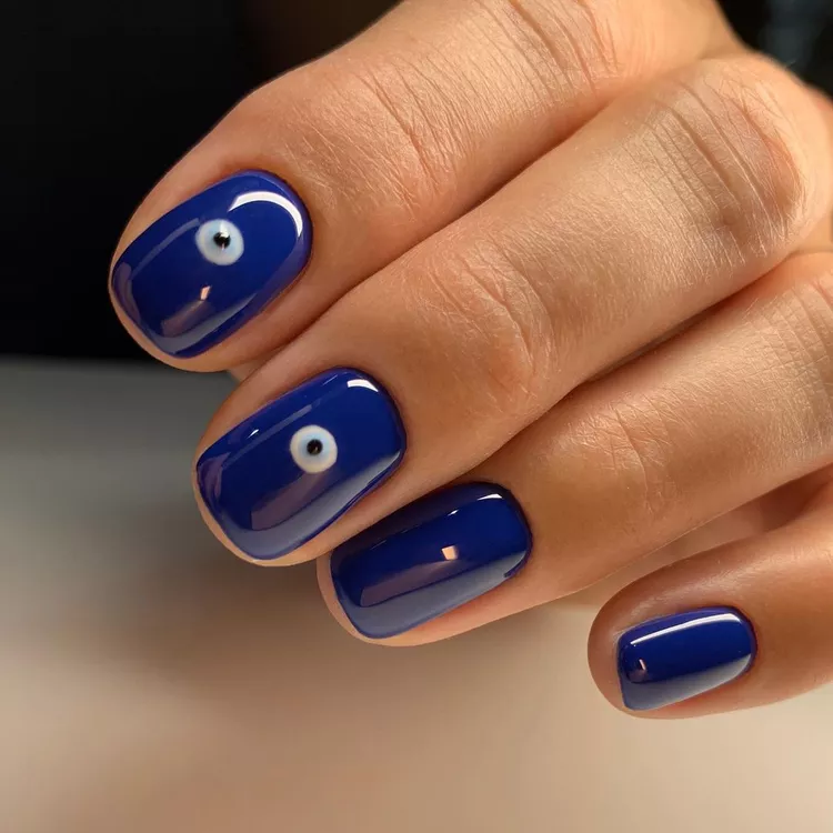 30 Stunning Dark Blue Nail Designs for a Denim-Inspired Summer Look 20 Glossy royal blue nail polish on short, rounded nails. Features white and black evil eye nail art accents on two fingers. A trendy spiritual nail design or DIY charm manicure idea.