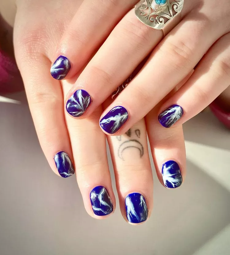 30 Stunning Dark Blue Nail Designs for a Denim-Inspired Summer Look 30 Electric blue lightning nail art on short oval nails. A unique and edgy abstract manicure design featuring white painted strokes over a deep blue base.
